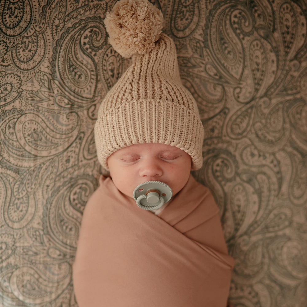 Mushie stretchy swaddle natural in-use sleepy baby close-up.