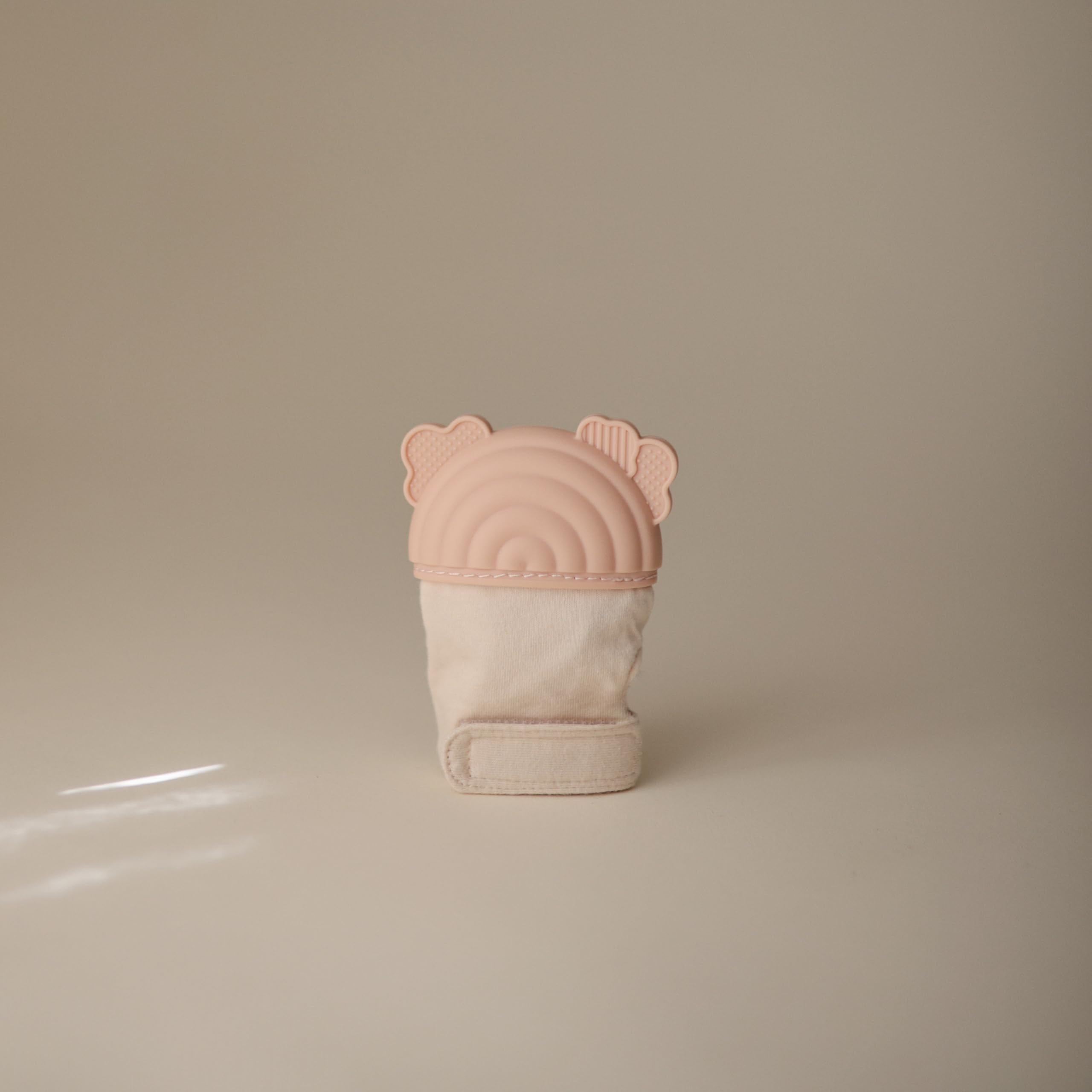 Mushie teething mitten rainbow on hand demonstrates hands-free soothing during playtime.