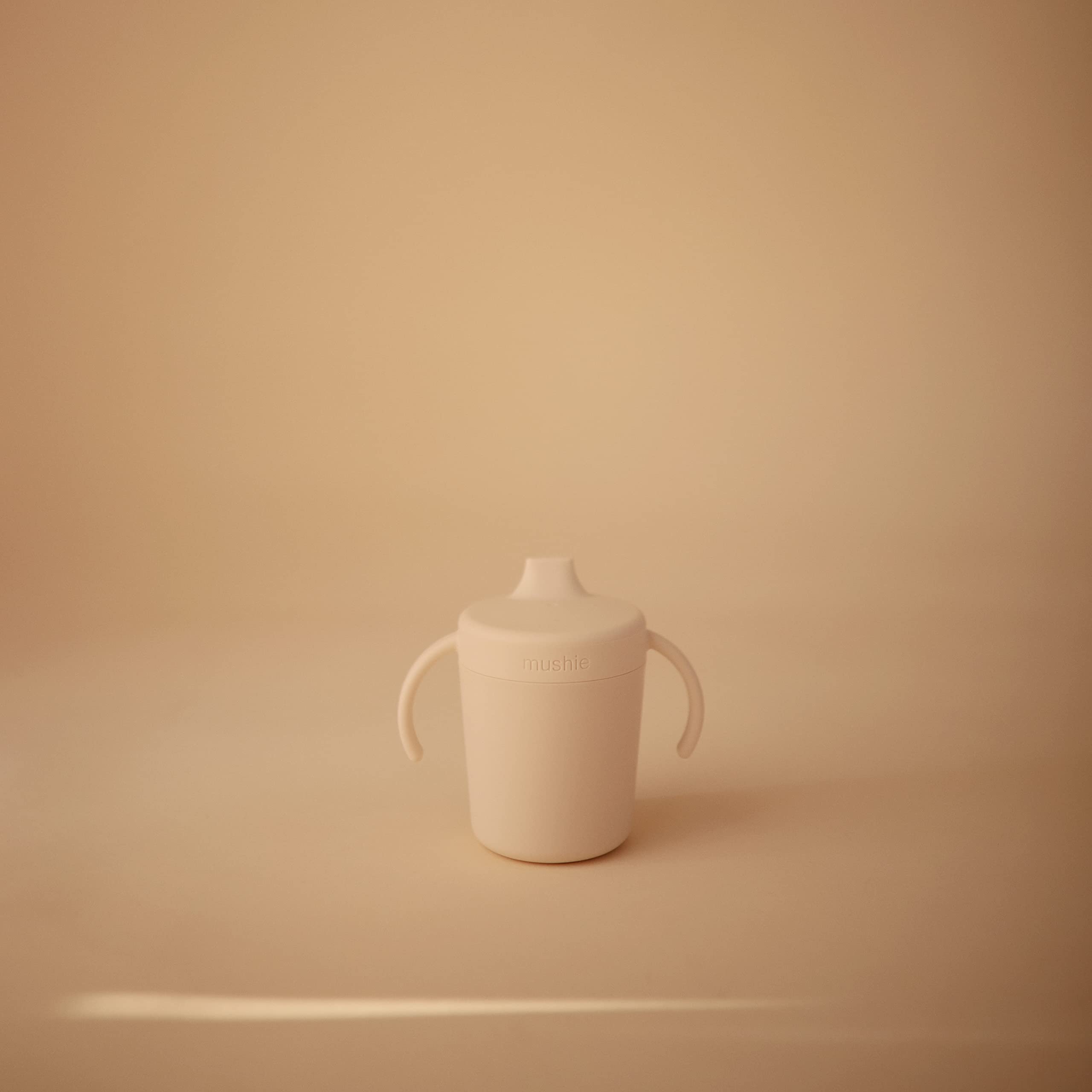 Mushie Trainer Sippy Cup Ivory handles grip for easy self-feeding.