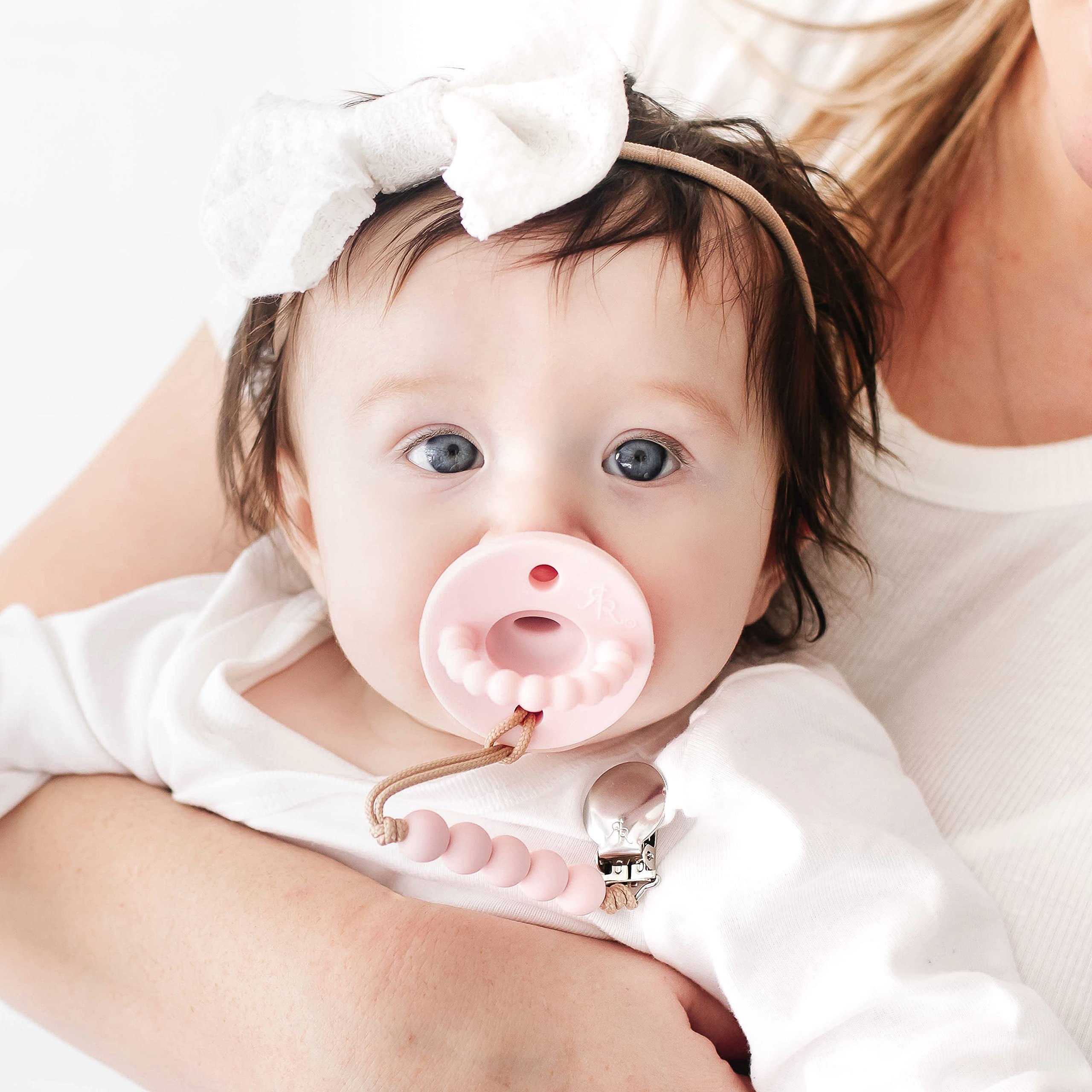 Baby uses Cutie PAT Flat Pink as teether while pacifier rests nearby