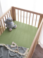 TILLYOU forest-green crib sheet on mattress with snug wrap for standard crib.
