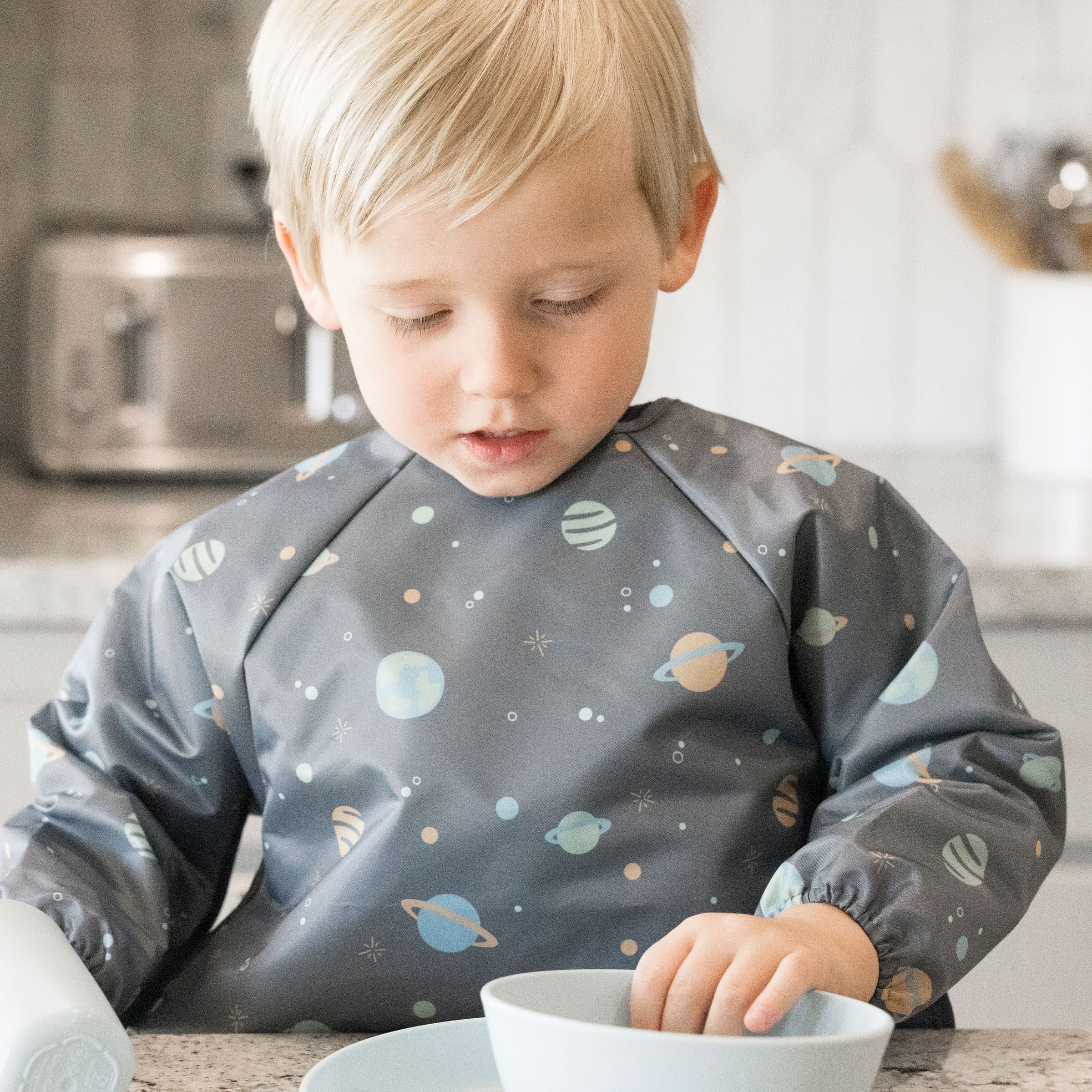 Tiny Twinkle long sleeve bib on child during mealtime demonstrates full-body coverage to protect clothing