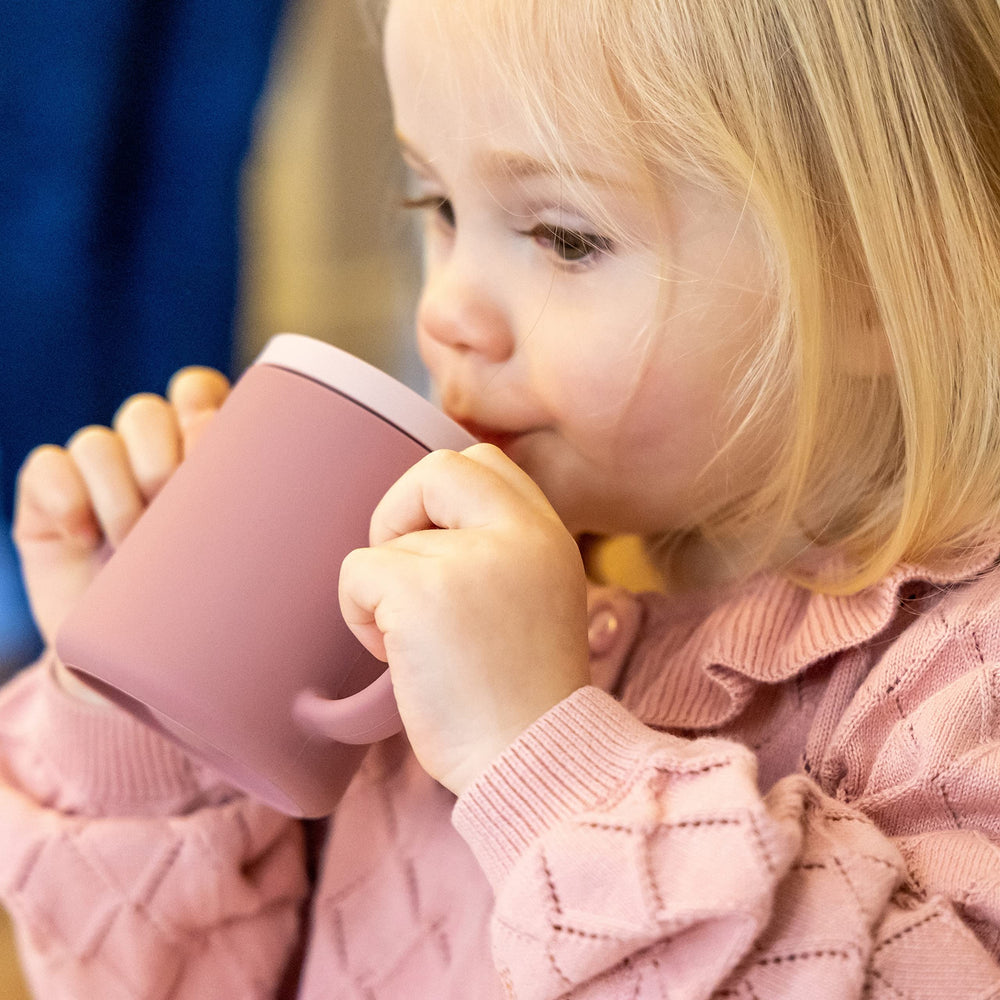 TUM TUM pink baby holding the trainer cup during mealtime practice.